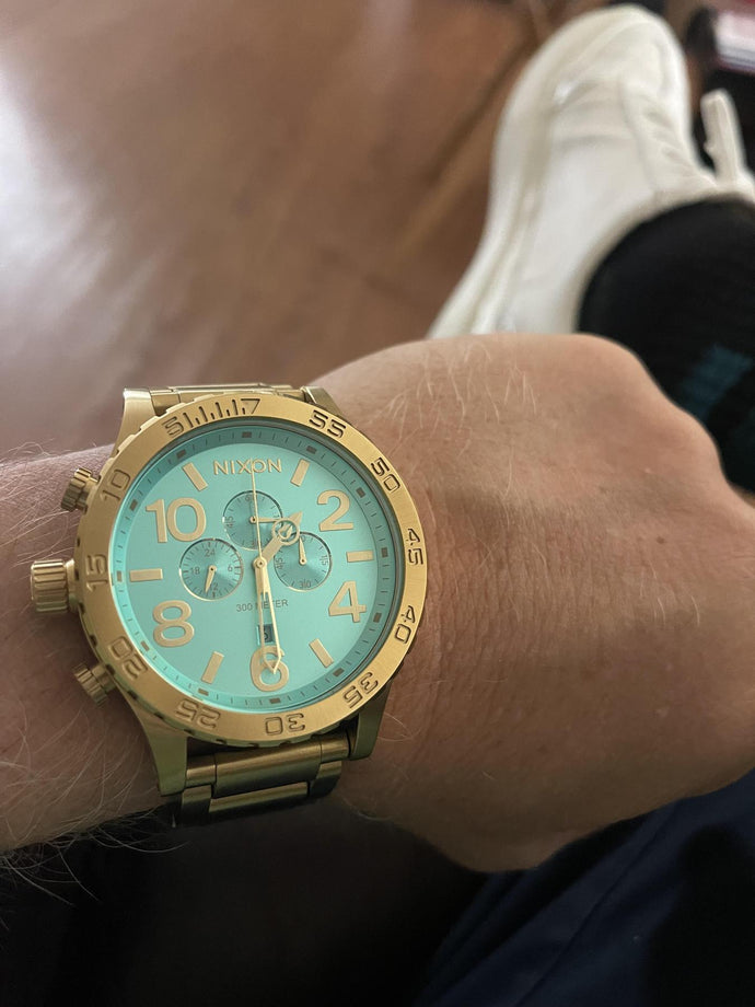 Gold watch with a turquoise face on a wrist, blurred background