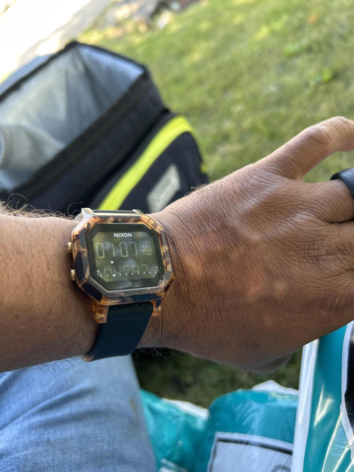 Hand wearing a Nixon digital watch with a grassy background