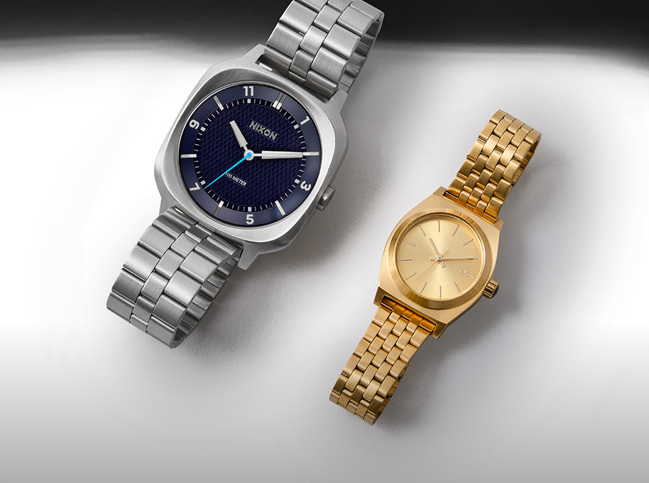 Two watches, one silver and one gold, on a light gray background