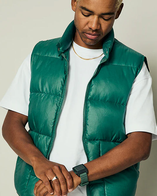 Man wearing a green puffer vest over a white shirt on a neutral background