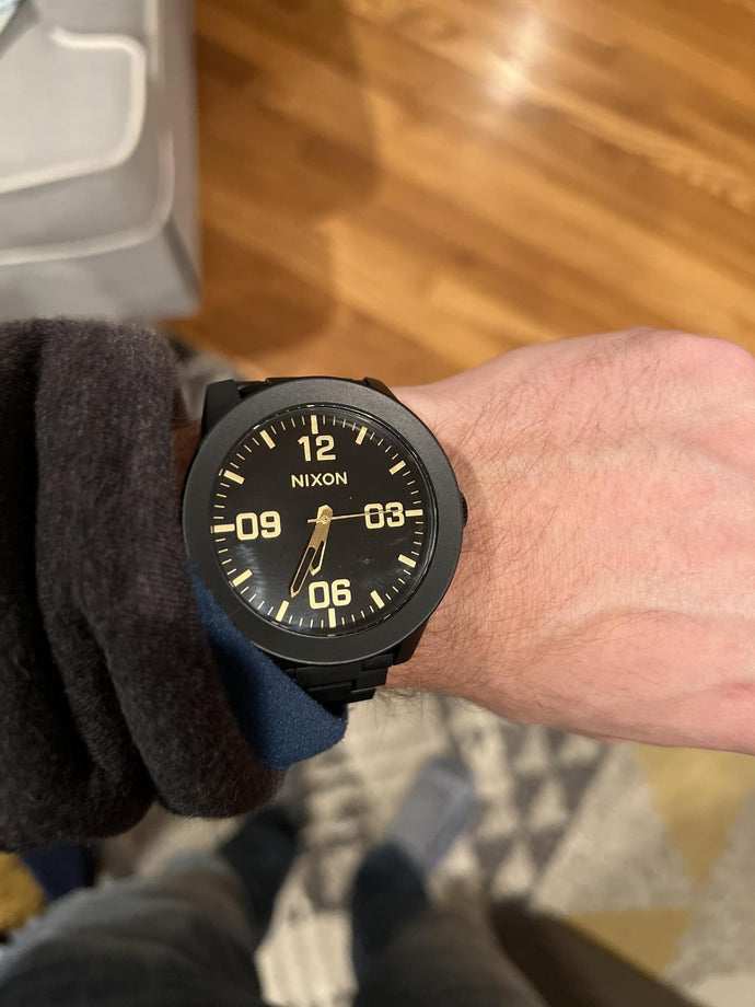 Person wearing a Nixon watch on a wooden floor.